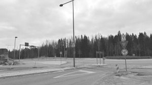 Black and white image of an empty roundabout with traffic signs and trees in the background.